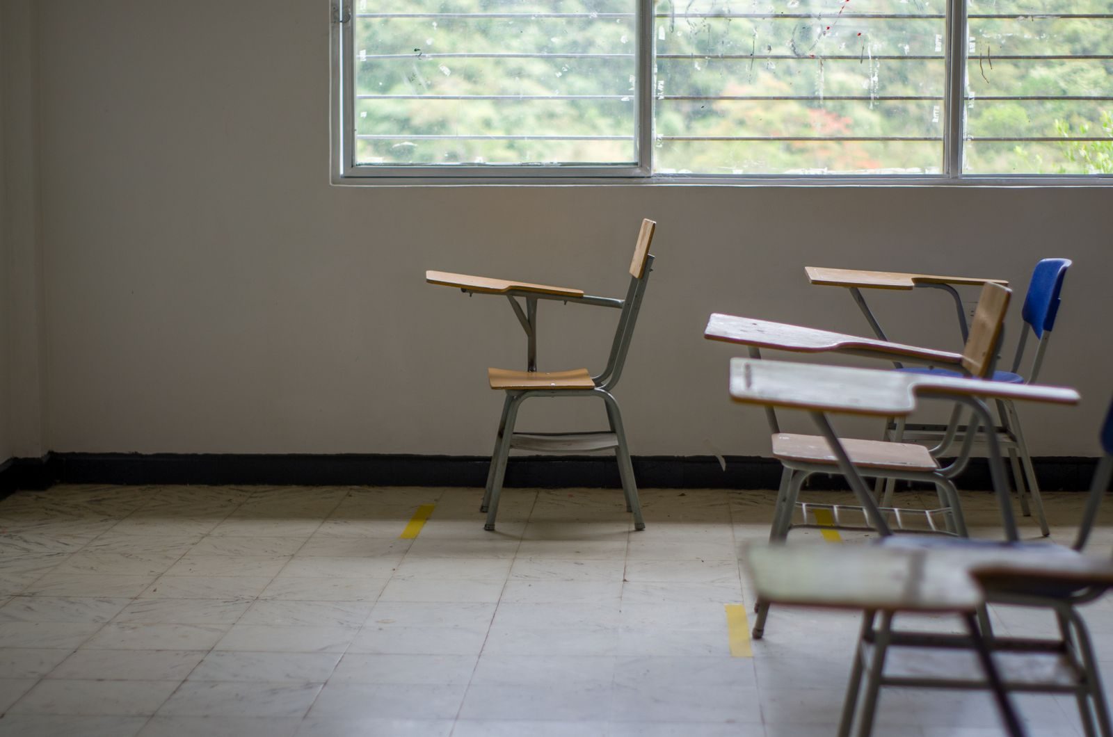 Quiet empty classroom interior with school desks by a large window.
