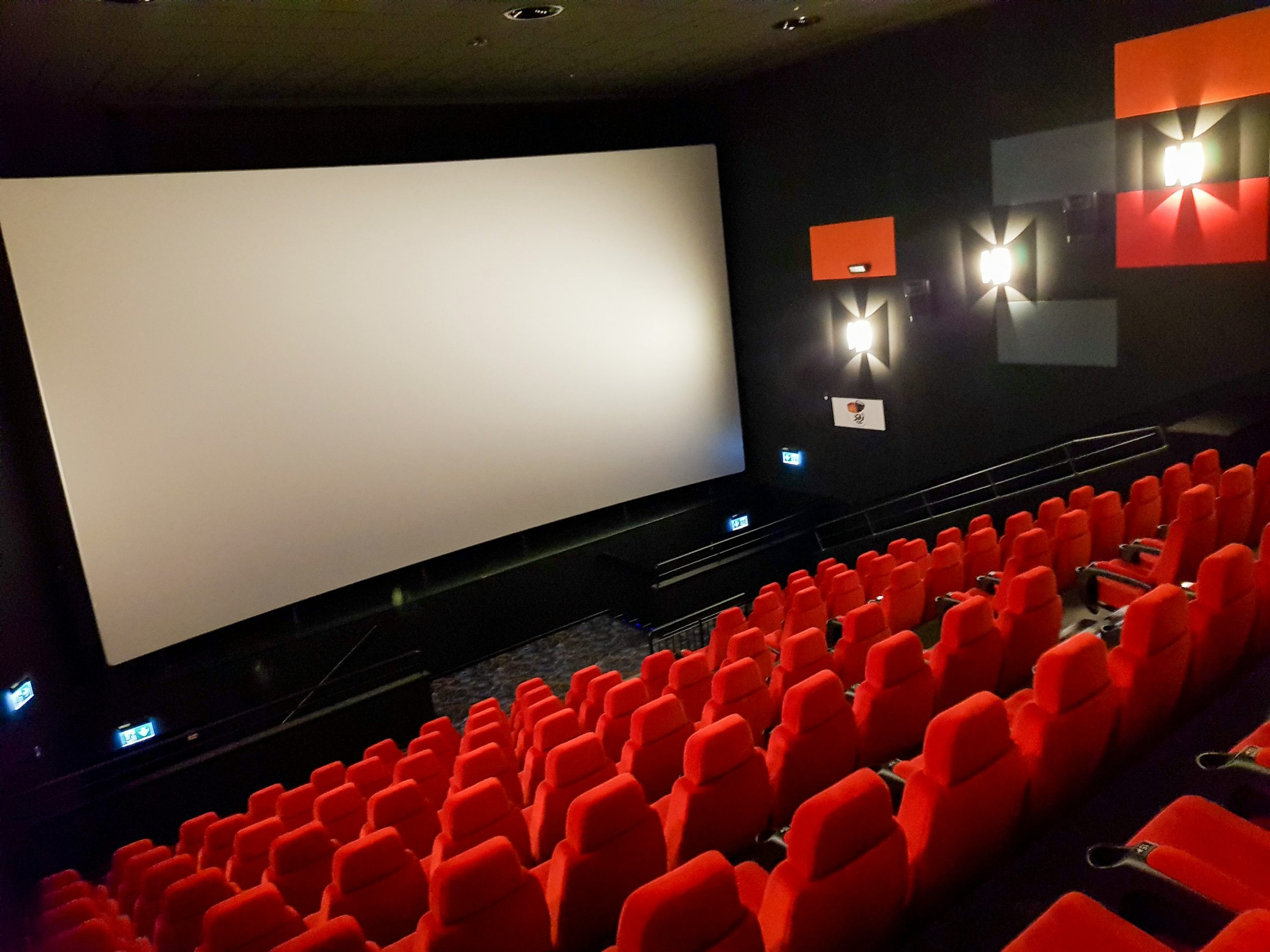 An empty movie theater with red seats facing a projector screen