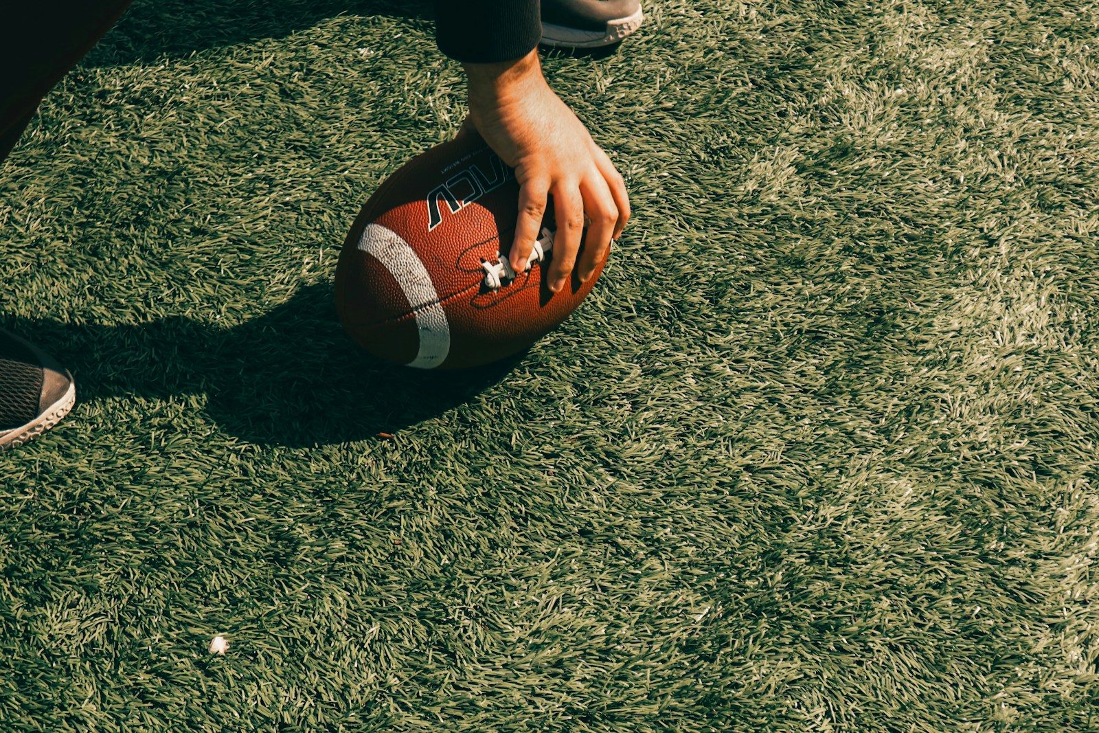 A person holding an american football on a grassy field
